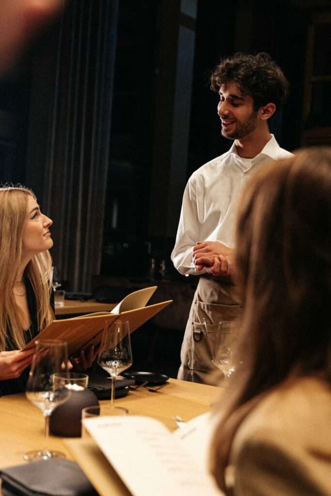 Eine Bediendung des 15 High steht am Tisch und berät eine Kundin mit Speisekarte in der Hand