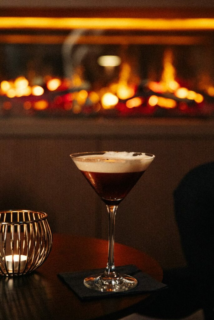 An espresso martini is placed on a table with a tea light in front of the fireplace in the 15 High Bar