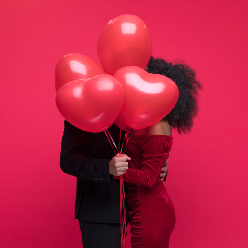 Paar umarmt sich hinter roten Herzballons vor rotem Hintergrund, romantische Atmosphäre im 15 High Restaurant & Bar.